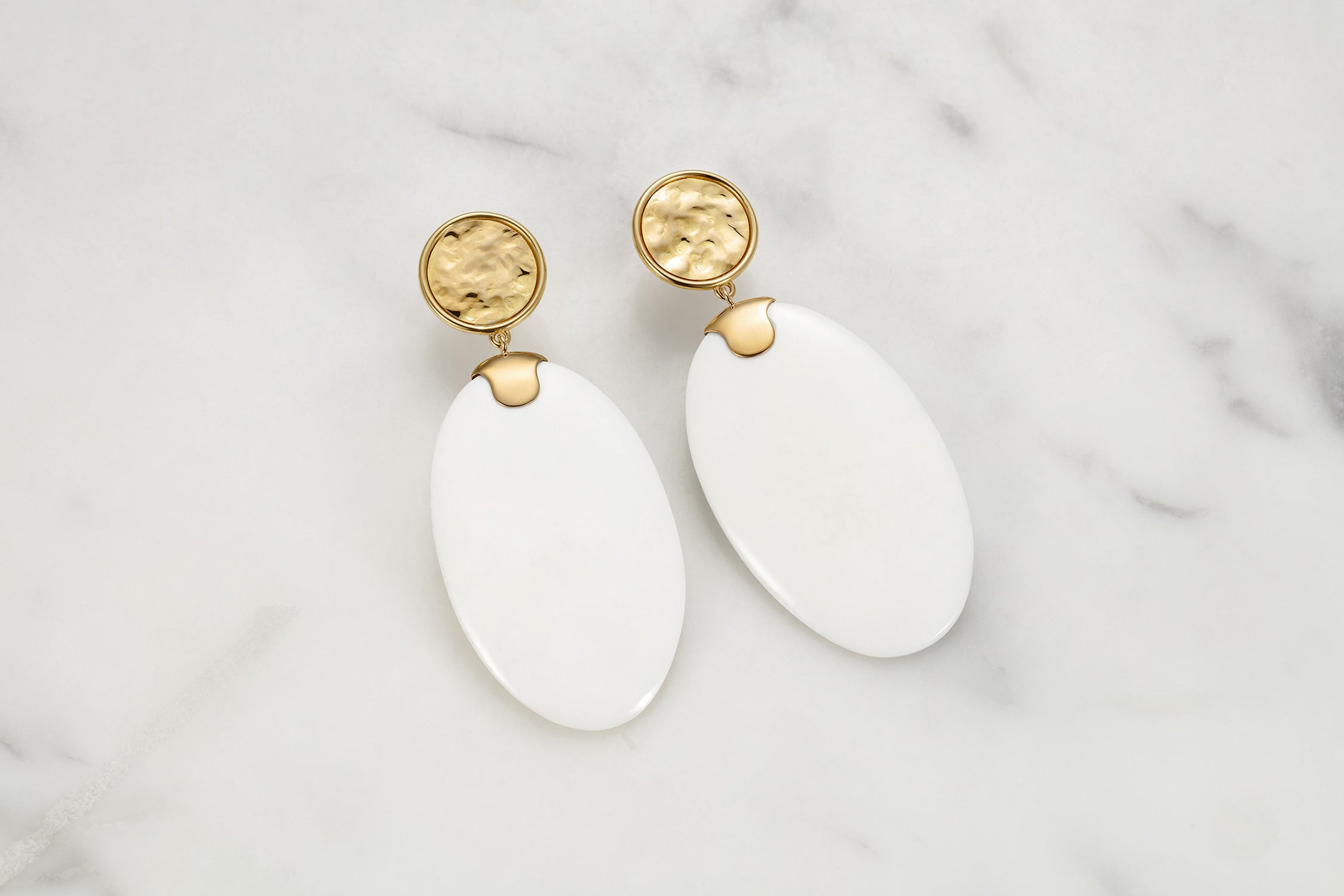 White carved earrings with 18k gold accents on a marble background by Isabella Roux