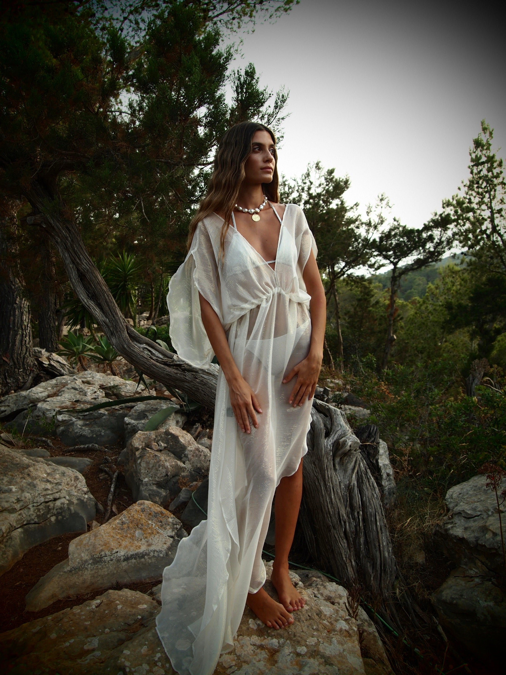Woman in a white dress standing on rocks with a forest background wearing Isabella Roux Baroque Pearl Necklace.