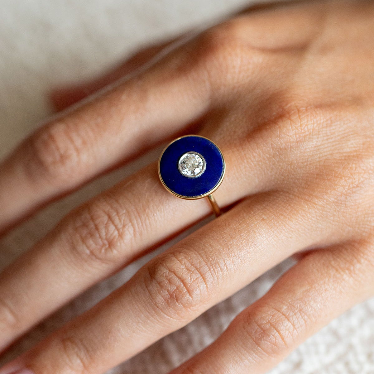 Close-up of a hand wearing a bespoke ring with a carved lapis and central diamond by Isabella Roux