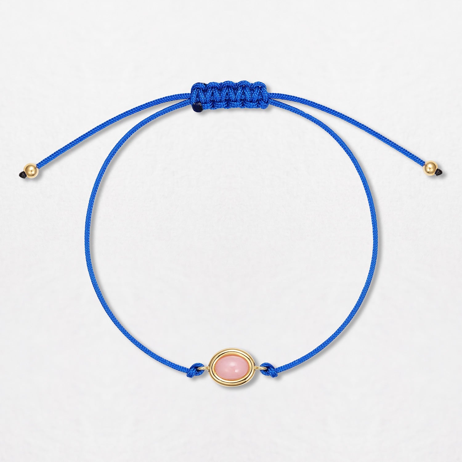 A Pink Opal Pebble Bracelet with a 0.65ct baby pink opal cabochon. Set in 18K yellow gold with gold beads on a single blue cord, with an adjustable slider fastening.