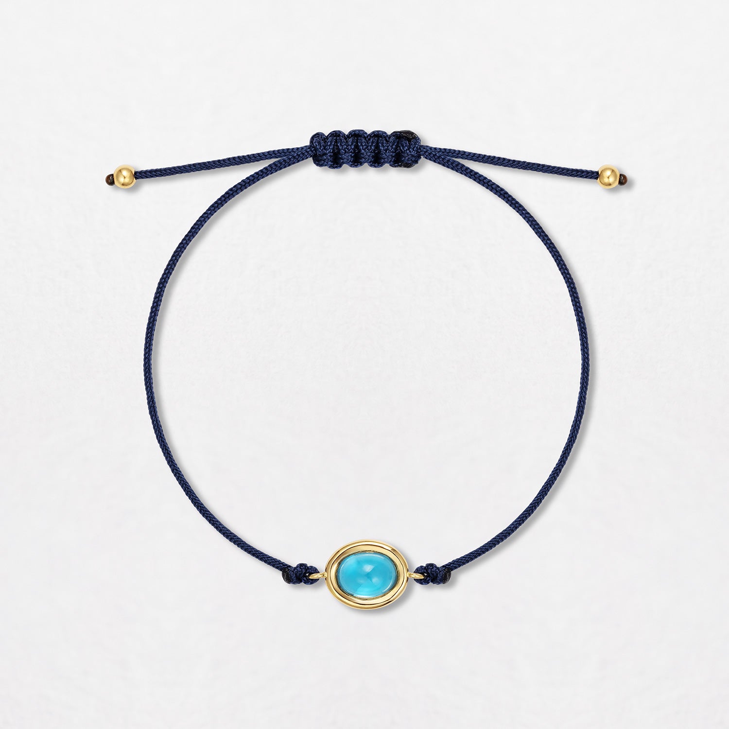 A Sky Blue Topaz Pebble Bracelet with a 2ct topaz cabochon. Set in 18K yellow gold with gold beads on a single navy blue cord, with an adjustable slider fastening.