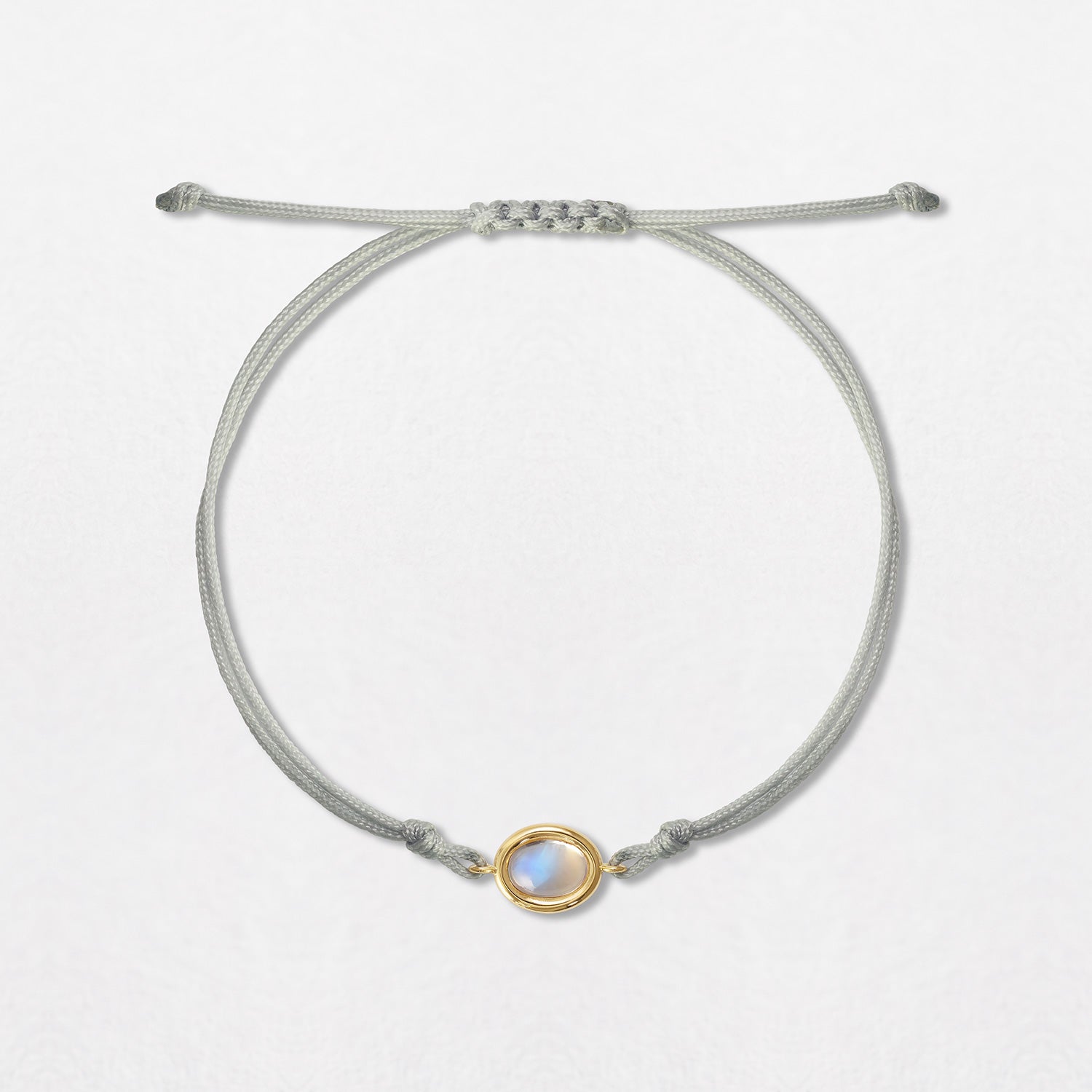 A Moonstone Pebble Bracelet with a 2ct oval moonstone cabochon. Set in 18K yellow gold on a double grey cord, with an adjustable slider fastening.