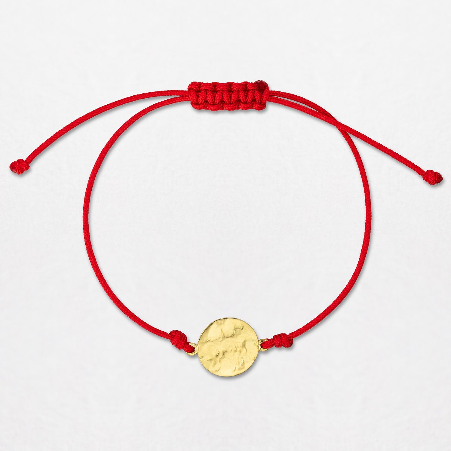 A Sun Disc Cord Bracelet, handbeaten in 18K yellow gold, on a red cord, with an adjustable slider fastening. The diameter of the disc is 11mm.