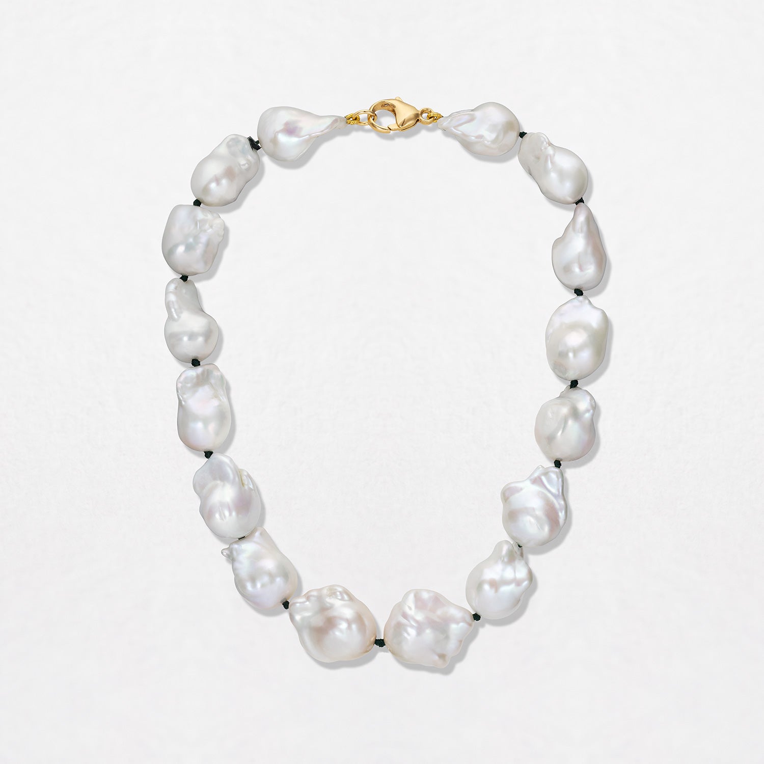 A Baroque Pearl Necklace with a set of baroque white freshwater pearls, strung and knotted on green thread, with an 18K yellow gold clasp. Total necklace length is 16".