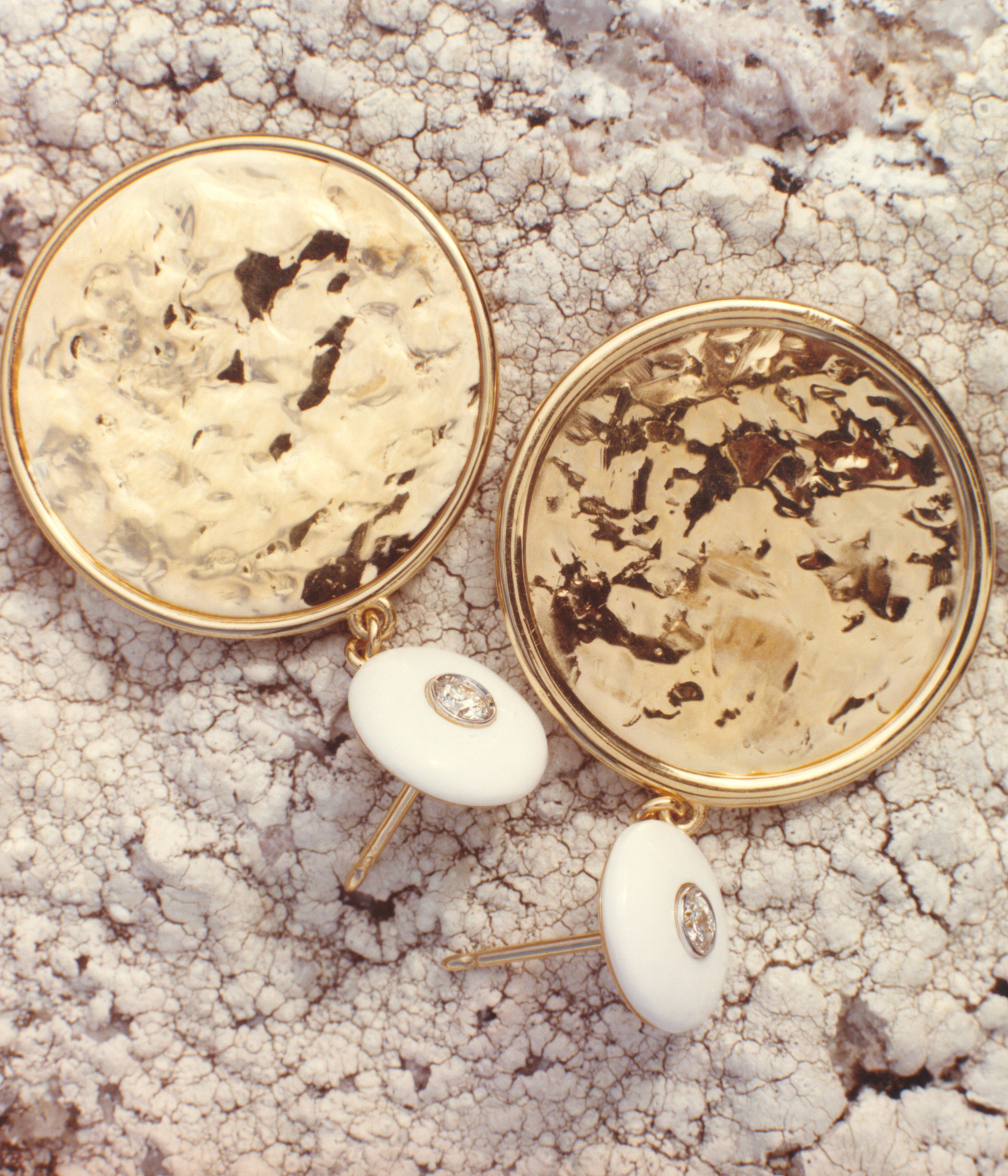 Pair of unique 18k gold earrings with carved white opal pebbles on a textured surface by Isabella Roux