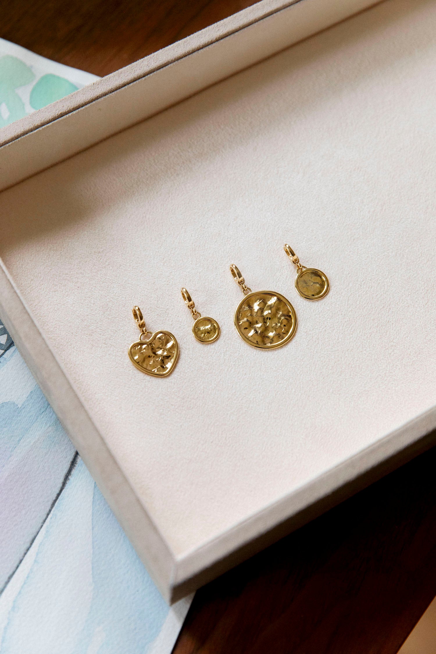 18k beaten gold sun disc pendants on a textured beige surface by Isabella Roux