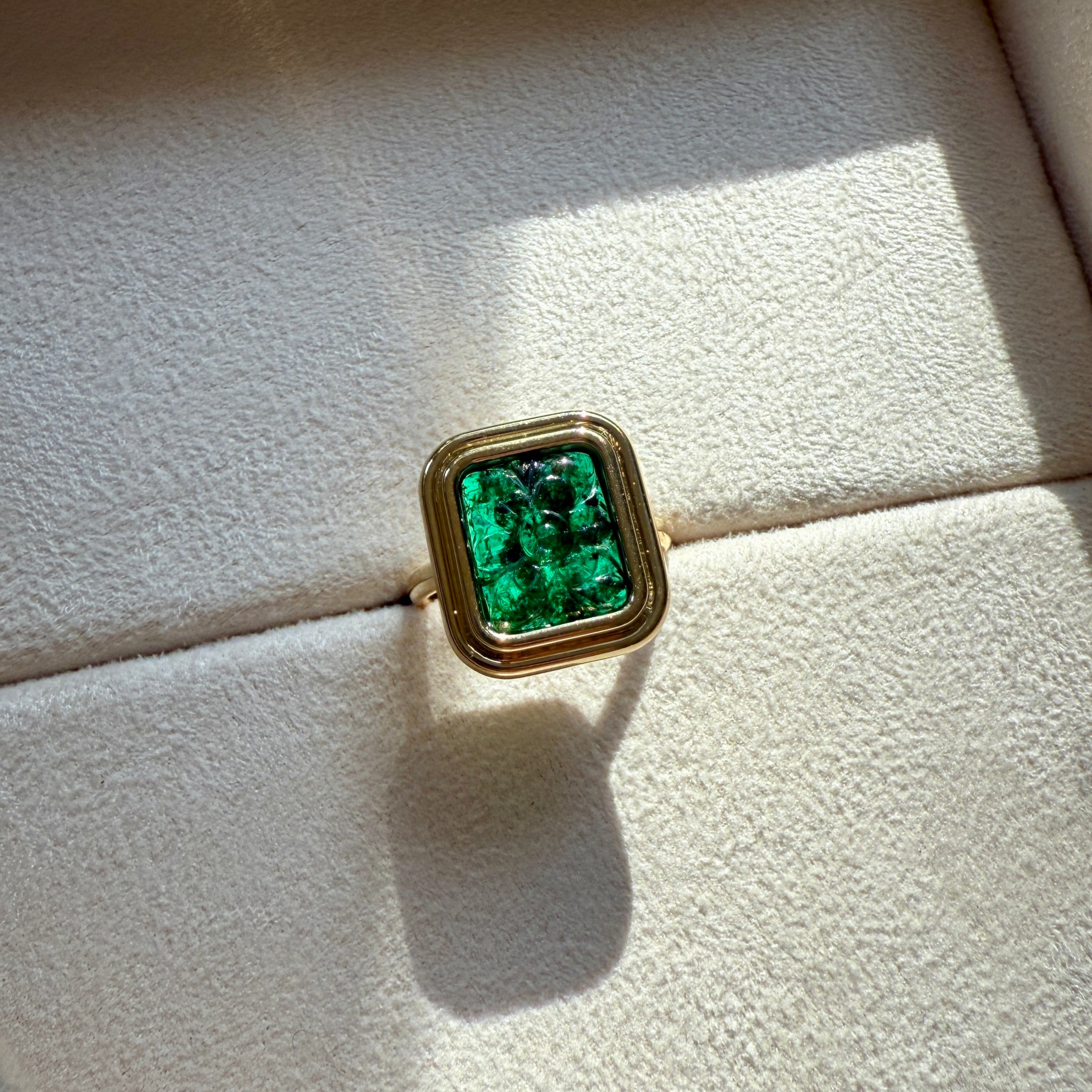 Bespoke 18k yellow gold ring with a carved green gemstone on a textured surface by Isabella Roux