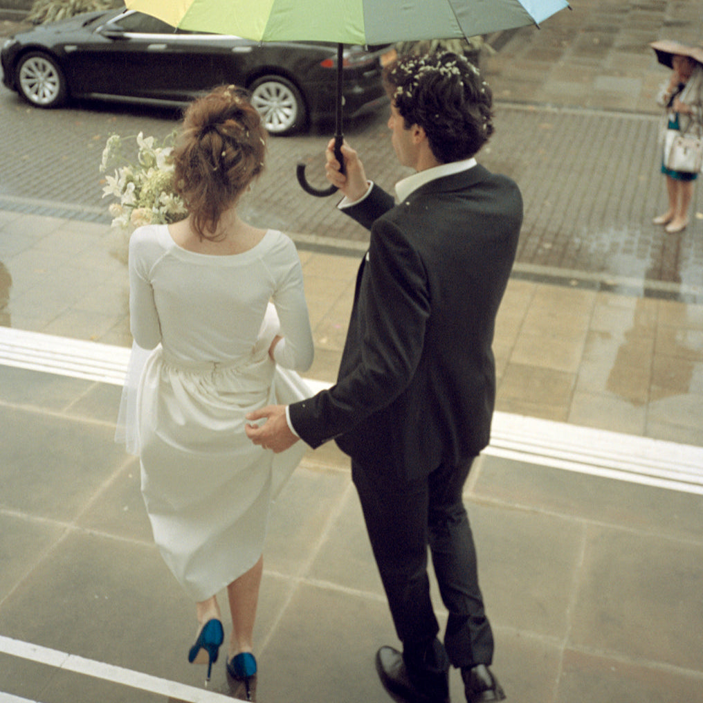 Isabella Roux and her husband holding hands under an umbrella on a their wedding day.