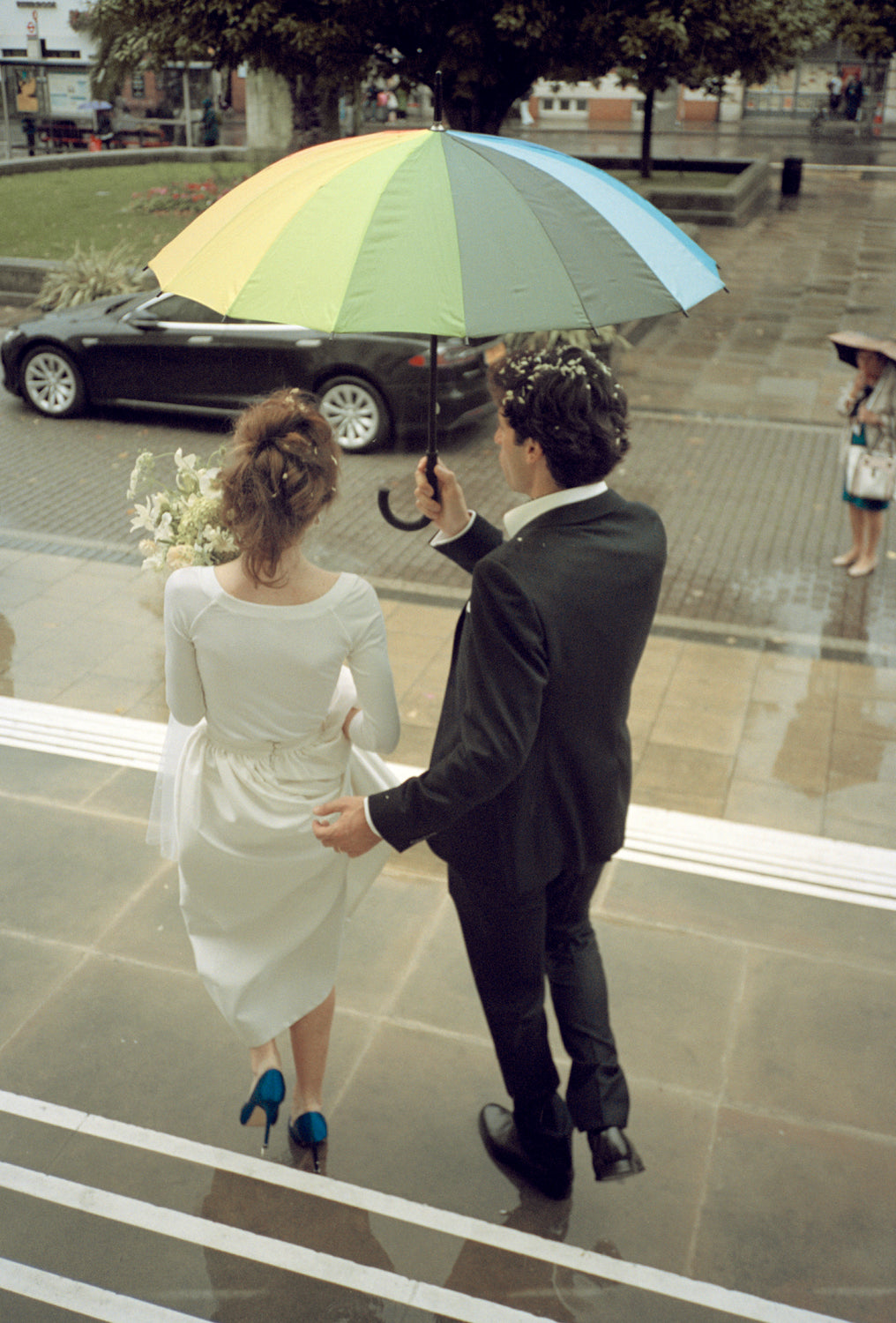 Sadhbh Isabella Roux-Fouillet and her husband holding hands under a colorful umbrella on their wedding day