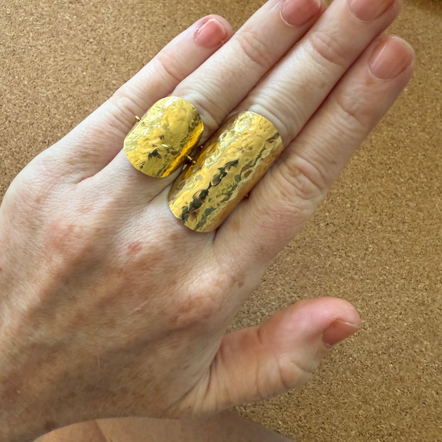 Hand with different 18K yellow gold Sun Shield Wrap Rings featuring hand-hammered gold sheet that wraps the finger by Isabella Roux