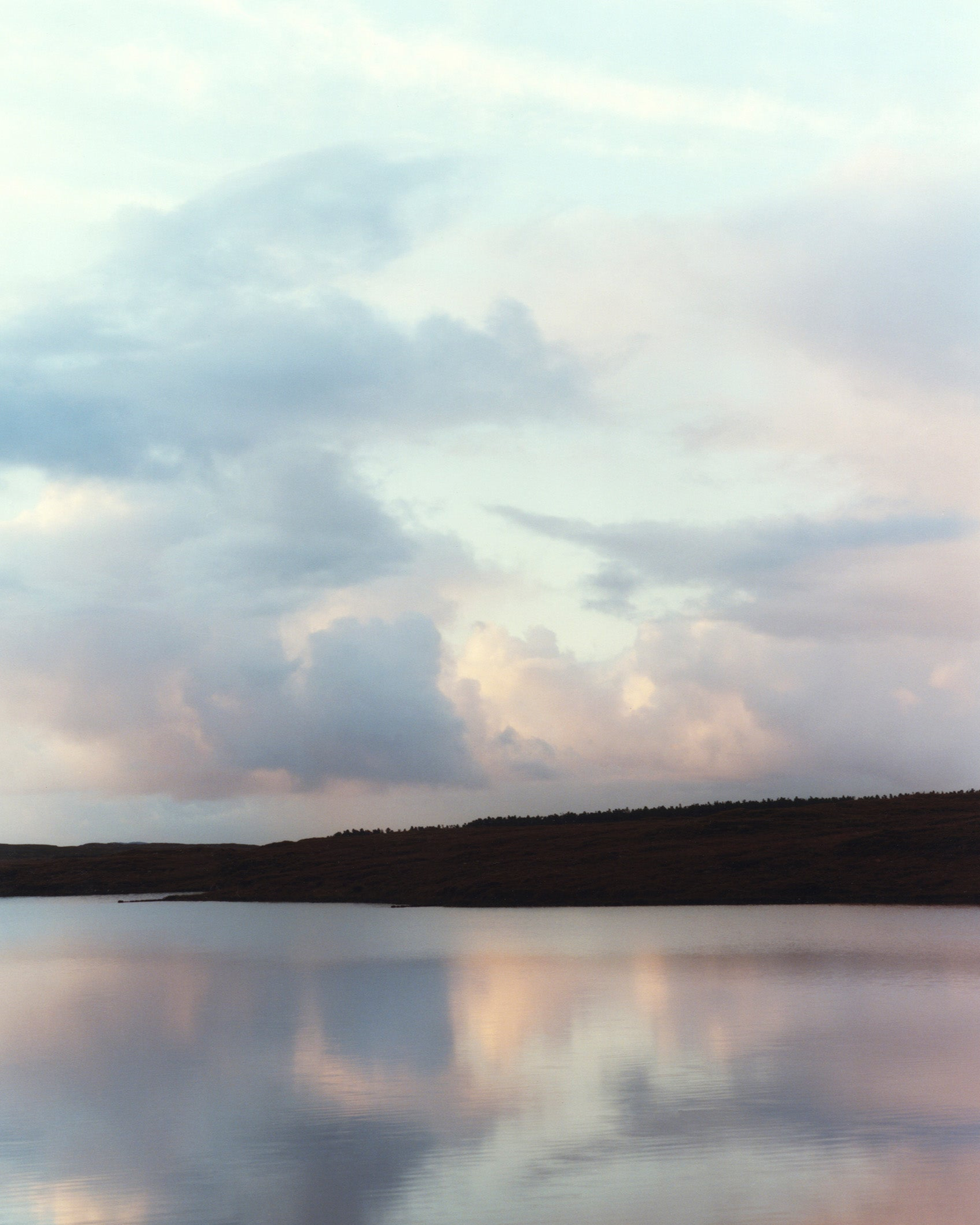 Cloudy sky reflected in a calm body of water with a distant shoreline in Ireland, from the Isabella Roux lookbook.
