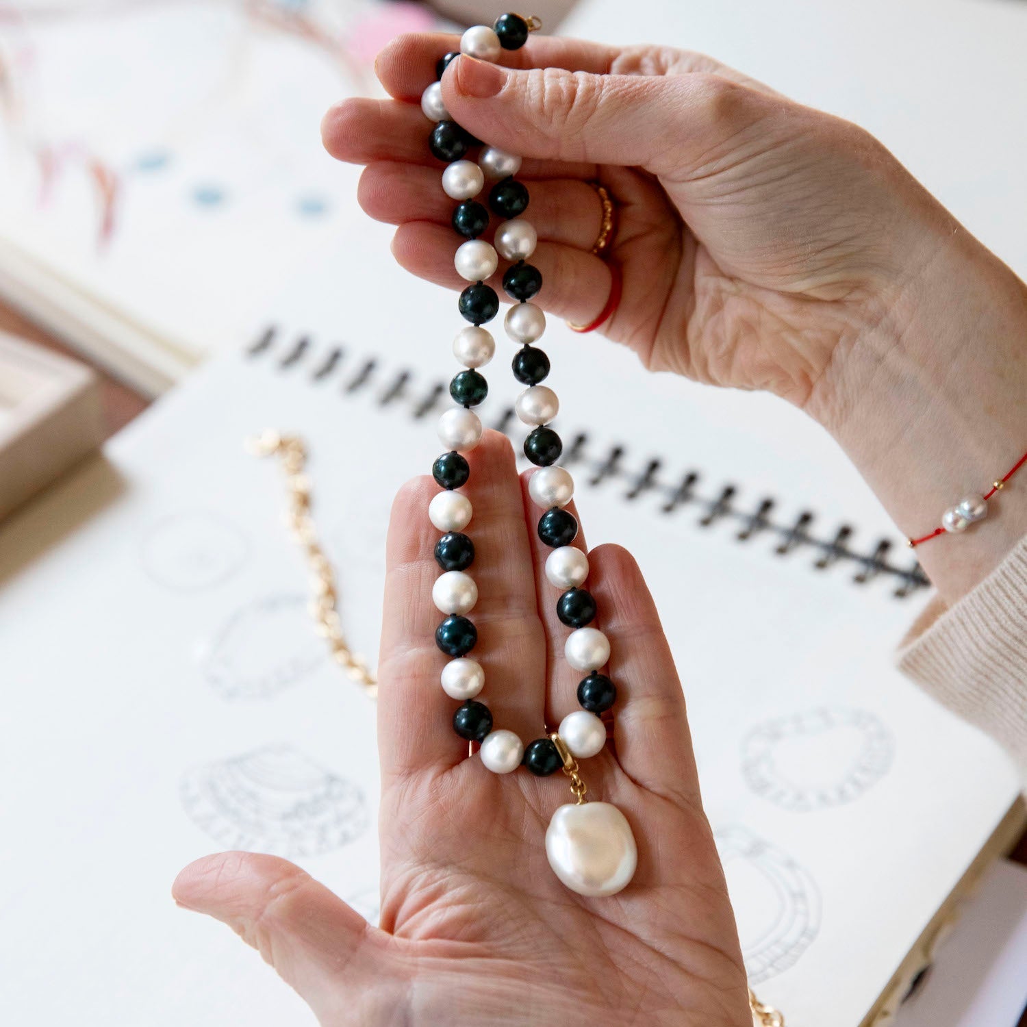 Person holding Pebble Monochrome Necklace featuring a set of black and white freshwater pearls knotted on navy thread with 18K yellow gold fittings by Isabella Roux