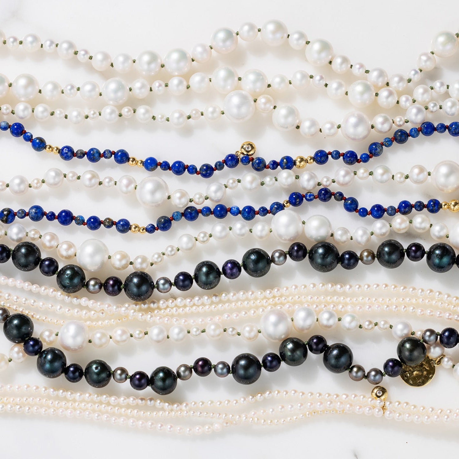 Multiple pearl and beaded necklaces on a white surface by Isabella Roux