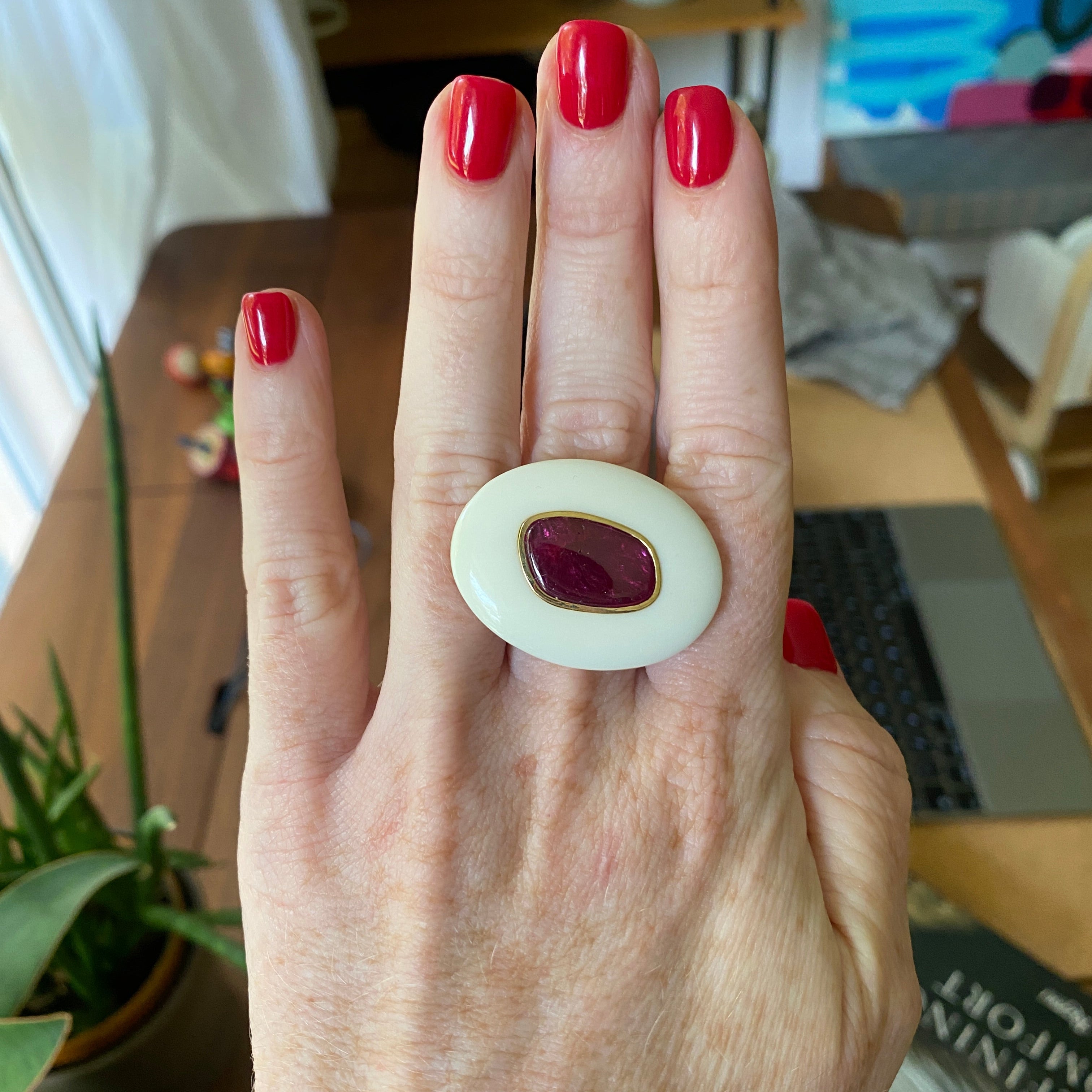 Hand wearing gorgeous 18K yellow gold Ruby & Opal Pebble Ring featuring a 5.23ct ruby slice surrounded by a hand-carved white opal by Isabella Roux.