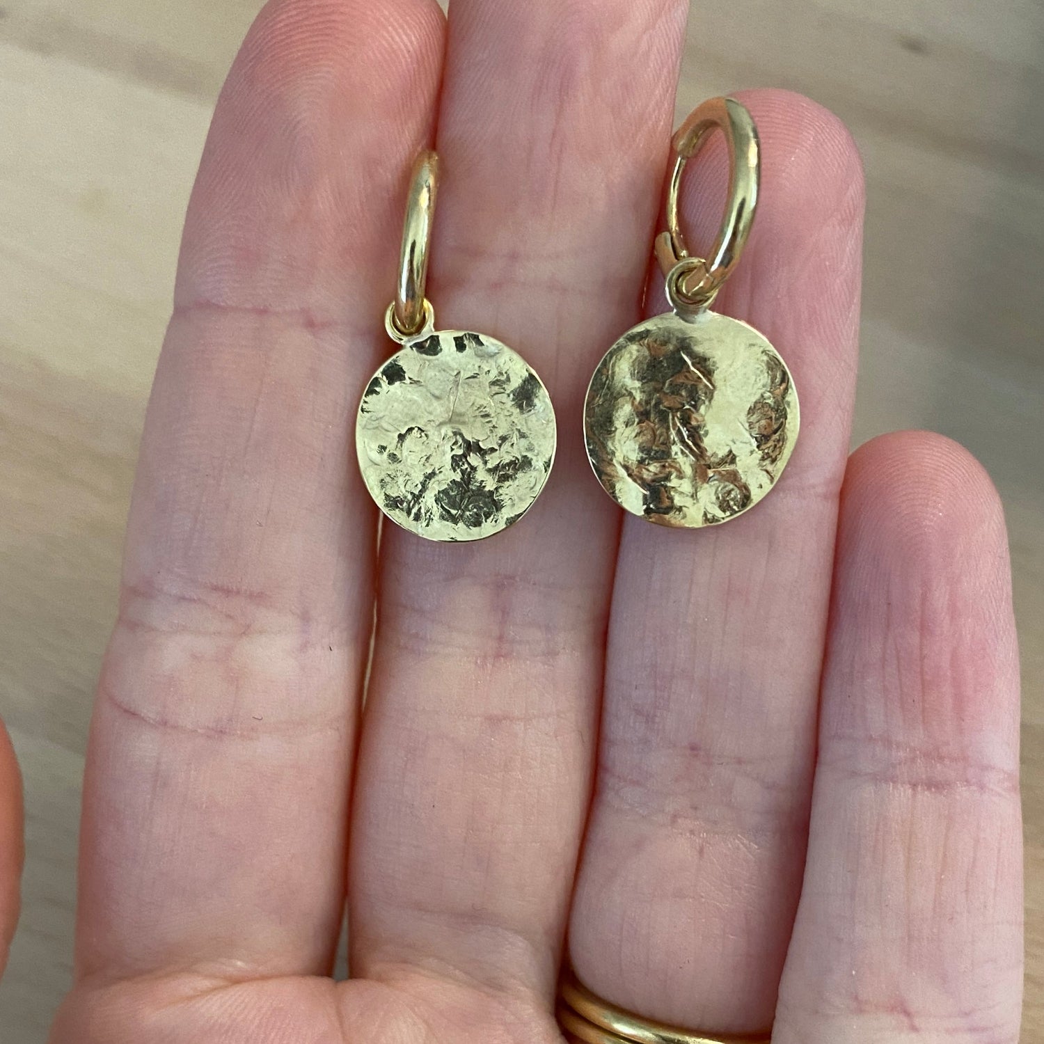 Hand with handcrafted 18K yellow gold Sun Disc Hoop Earrings featuring 12mm hoops with detachable 13mm handmade beaten gold discs by Isabella Roux.